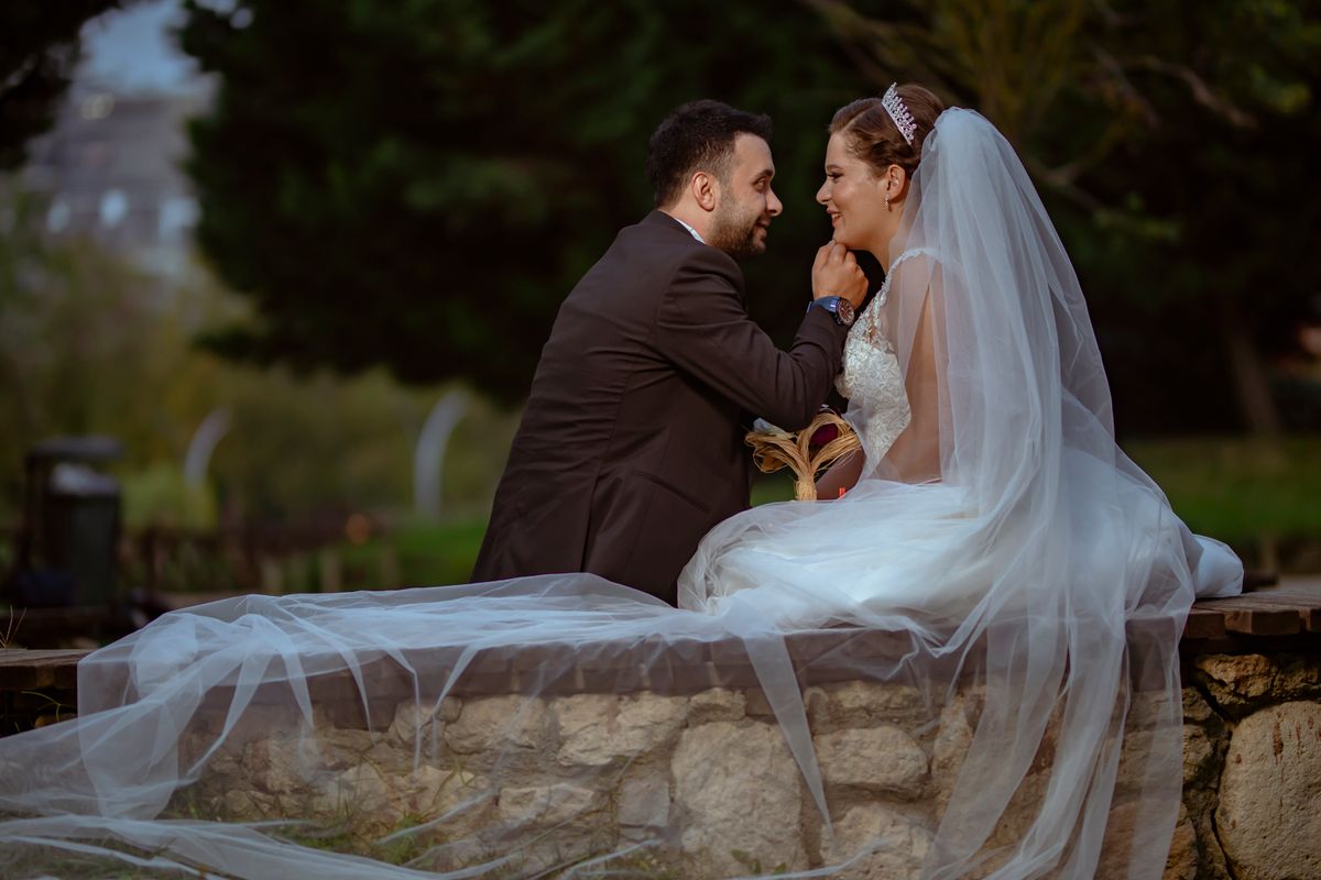 Ein Hochzeitspaar sitzt auf einer Steinmauer und lächelt sich an.